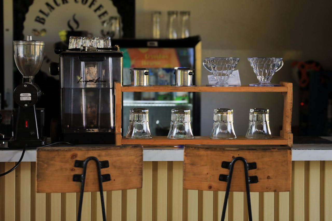 Meja konter kedai kopi yang nyaman dengan peralatan penyeduh kopi dan kursi kayu.